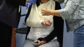 Two people assisting a person wearing a sling on their right arm.