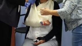 Two people assisting a person wearing a sling on their right arm.