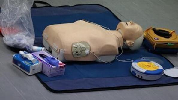 A resuscitation doll on the floor with other medical equipment including a defibrillator