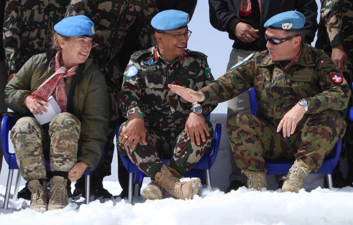 Two men and one woman military peacekeepers sit on chairs in the snow, chatting.