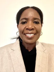 A woman stands in front of a white background, smiling for the camera